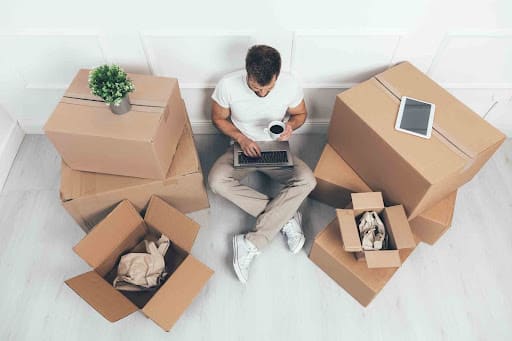 Man with coffee surrounded by moving boxes searching for renters insurance on a laptop.