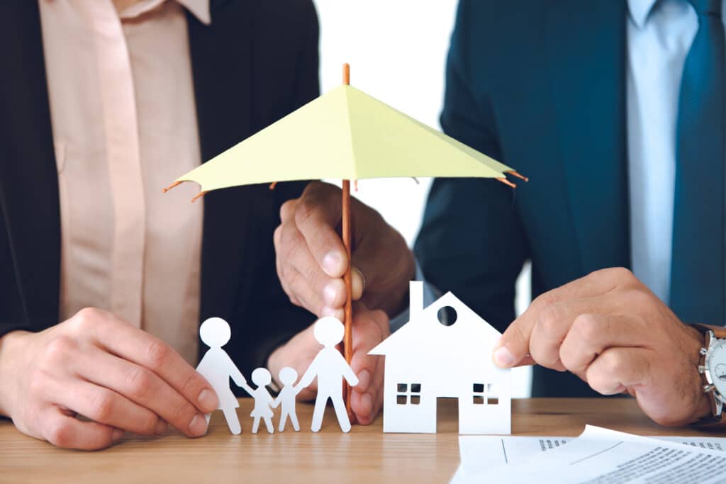 A cropped image of two insurance agents holding an umbrella over a family and their home representing umbrella insurance