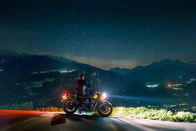 A person on a motorcycle looking out over a city in the dark with their lights shining