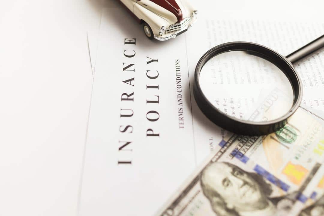 An insurance policy with a magnifying glass, money and a model car on top