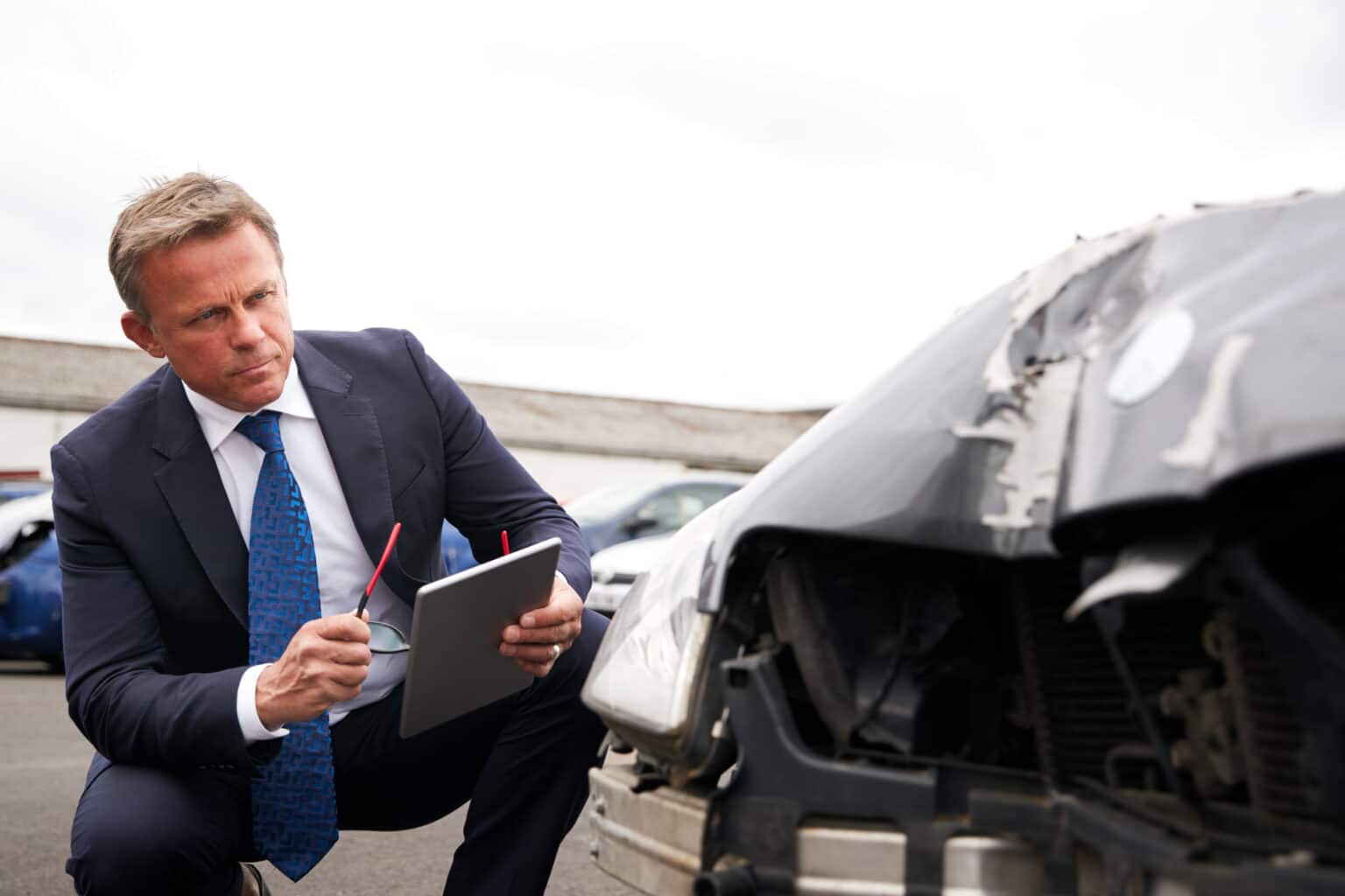 Male Insurance Loss Adjuster With Digital Tablet Inspecting Damage To Insurance agent assessing a car after an accident