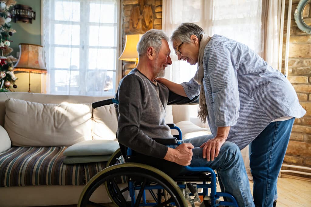Disability insurance concept with an elderly man in a wheelchair being embraced by his wife