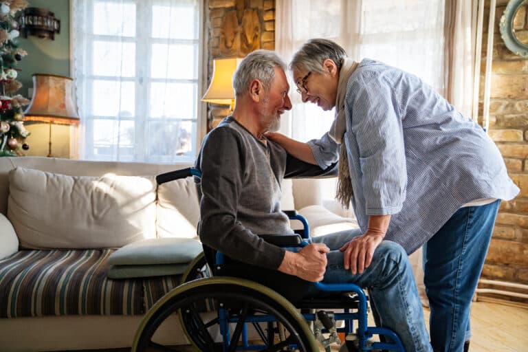 Disability insurance concept with an elderly man in a wheelchair being embraced by his wife