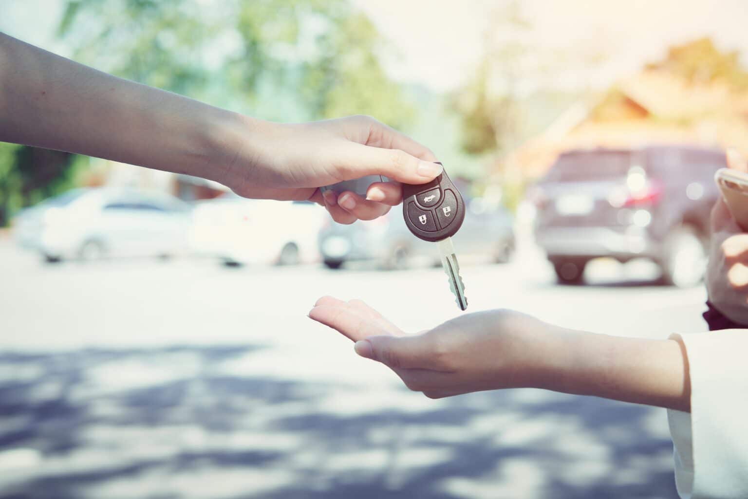Adding a driver to car insurance concept with a hand passing off a car key to another person reaching out to take