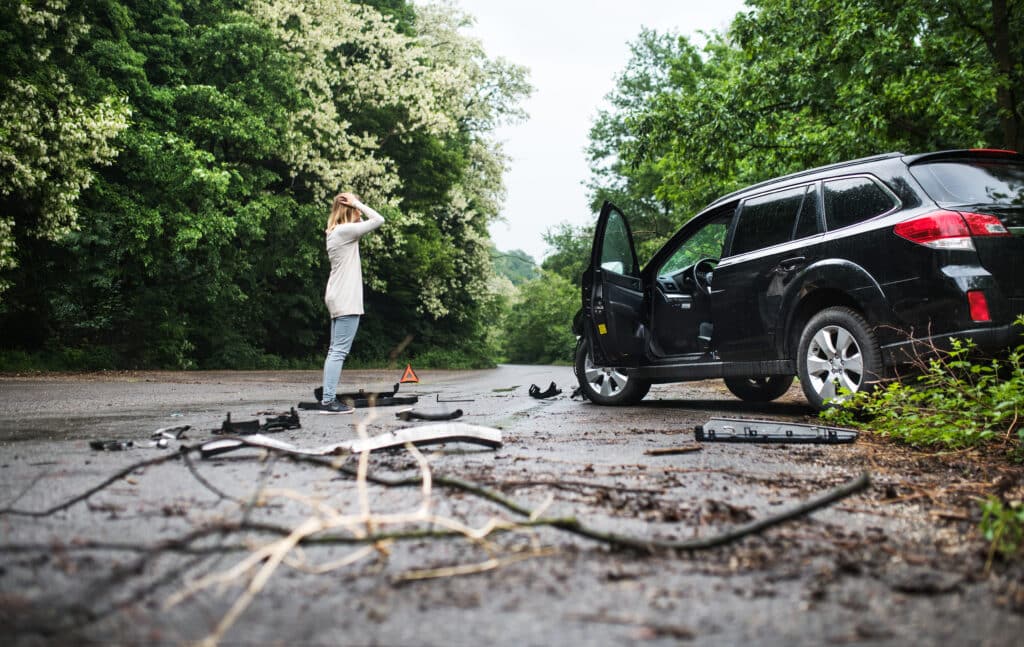 Woman upset in the road with a car that has been in an accident with a tree limb in the foreground