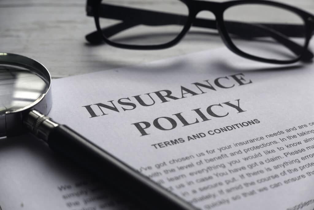 Selective focus of magnifying glass, glasses and Insurance Policy letter on a white wooden background.