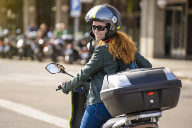 motorcycle insurance coverage concept with back side view portrait of a red-haired woman riding a motorcycle on a city street.