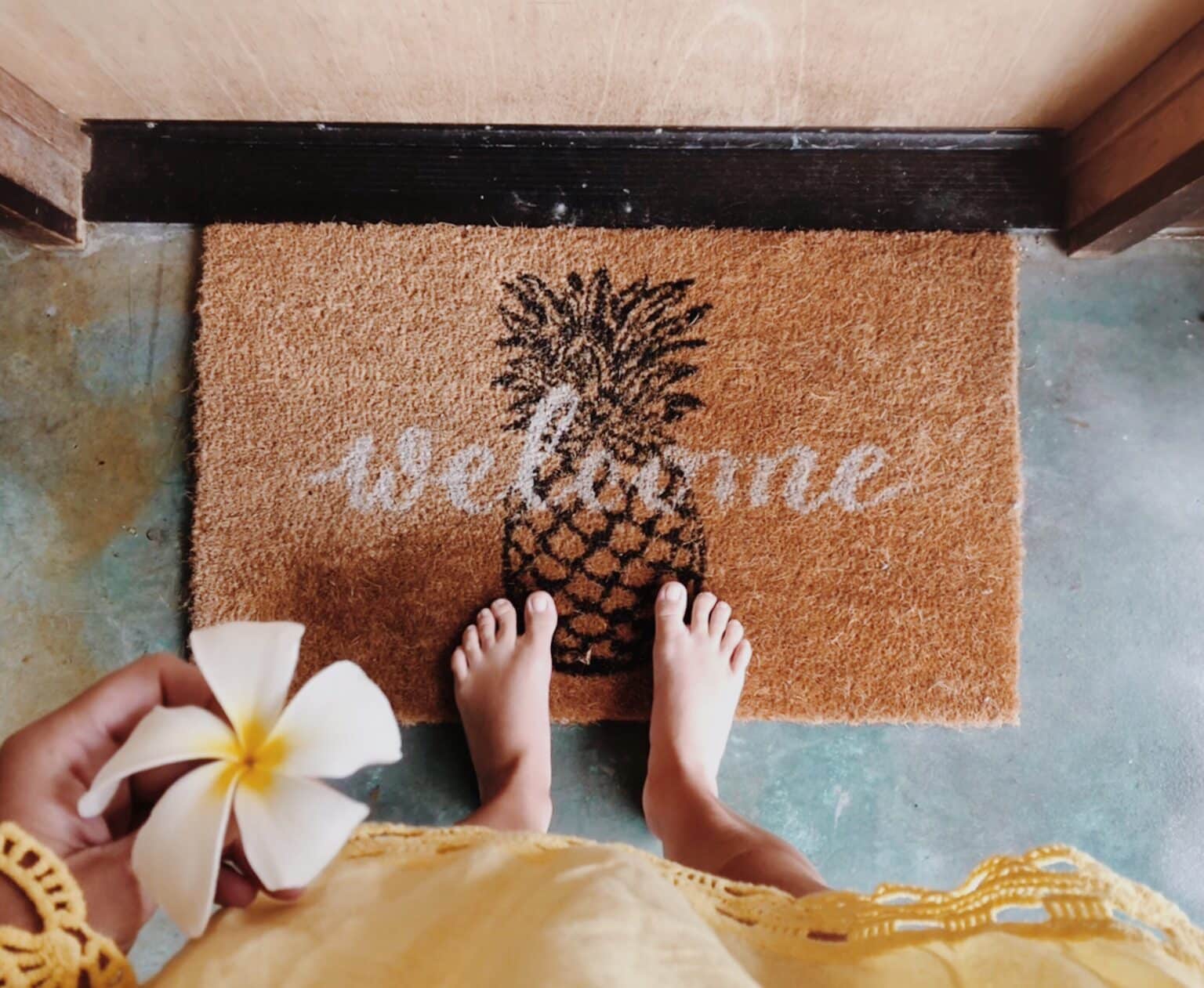 welcome mat at a vacation rental property with someone standing in front of the door in a beach coverup and a tropical flower.