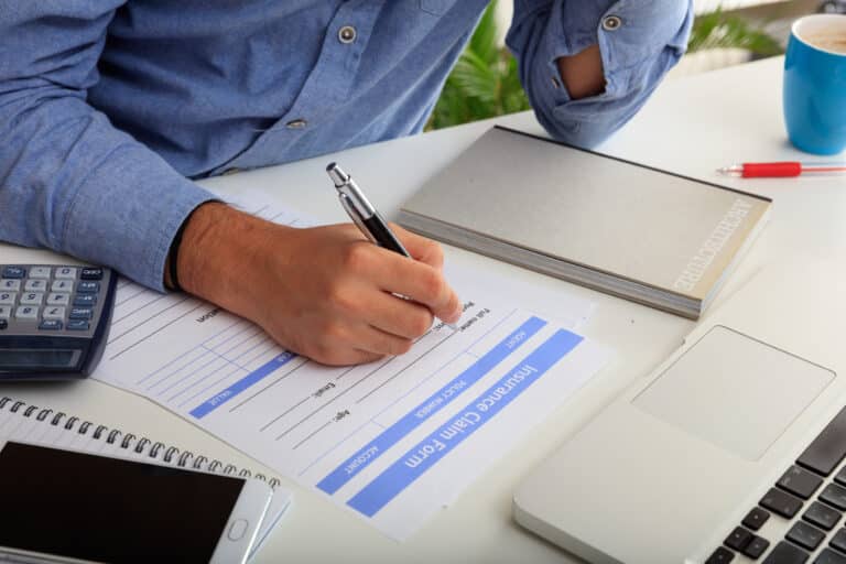 Man filling out a business Insurance Claims Form in an office background