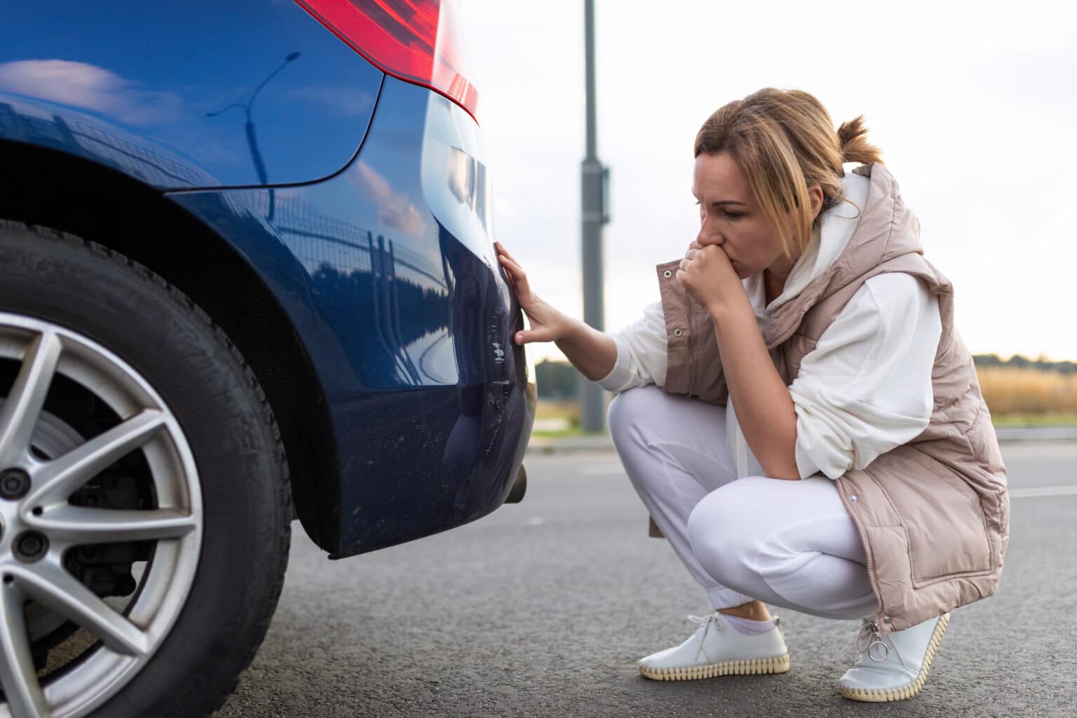 puzzled and annoyed woman looking at scratch on car bumper after minor car accident.