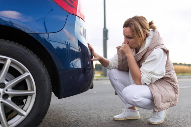 puzzled and annoyed woman looking at scratch on car bumper after minor car accident.