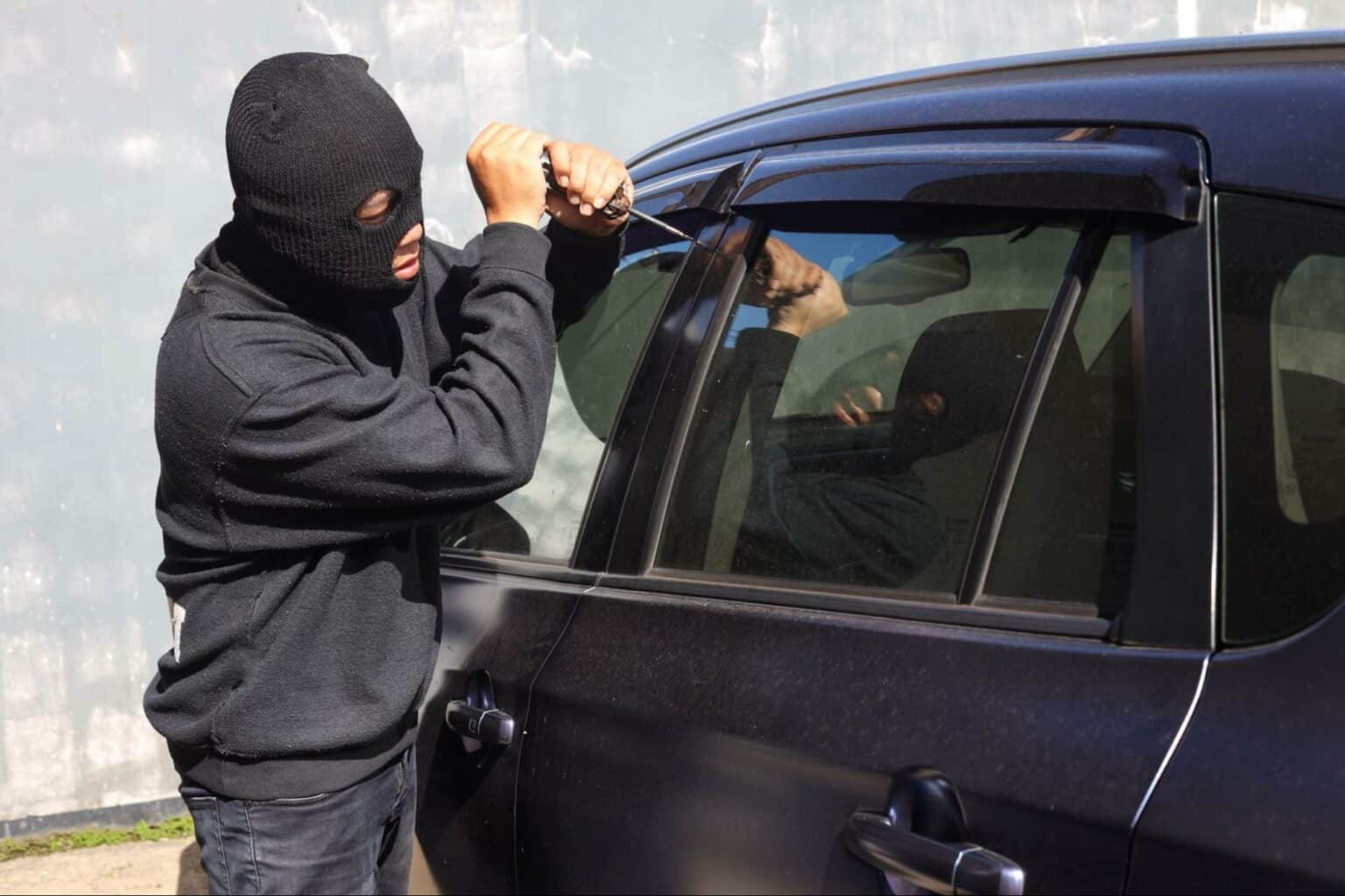 Burglar attempting to break into a parked car using a tool.