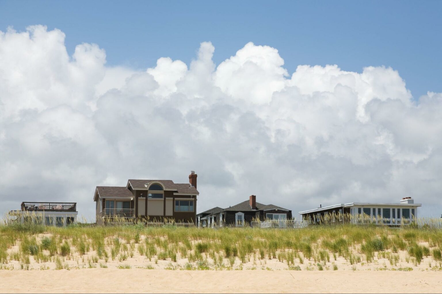 Charming beachfront homes lined against sandy dunes and a bright blue sky.