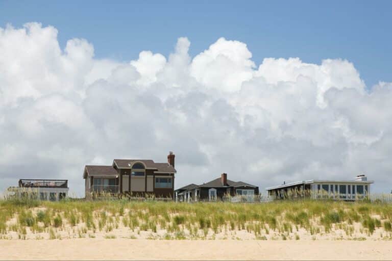 Charming beachfront homes lined against sandy dunes and a bright blue sky.