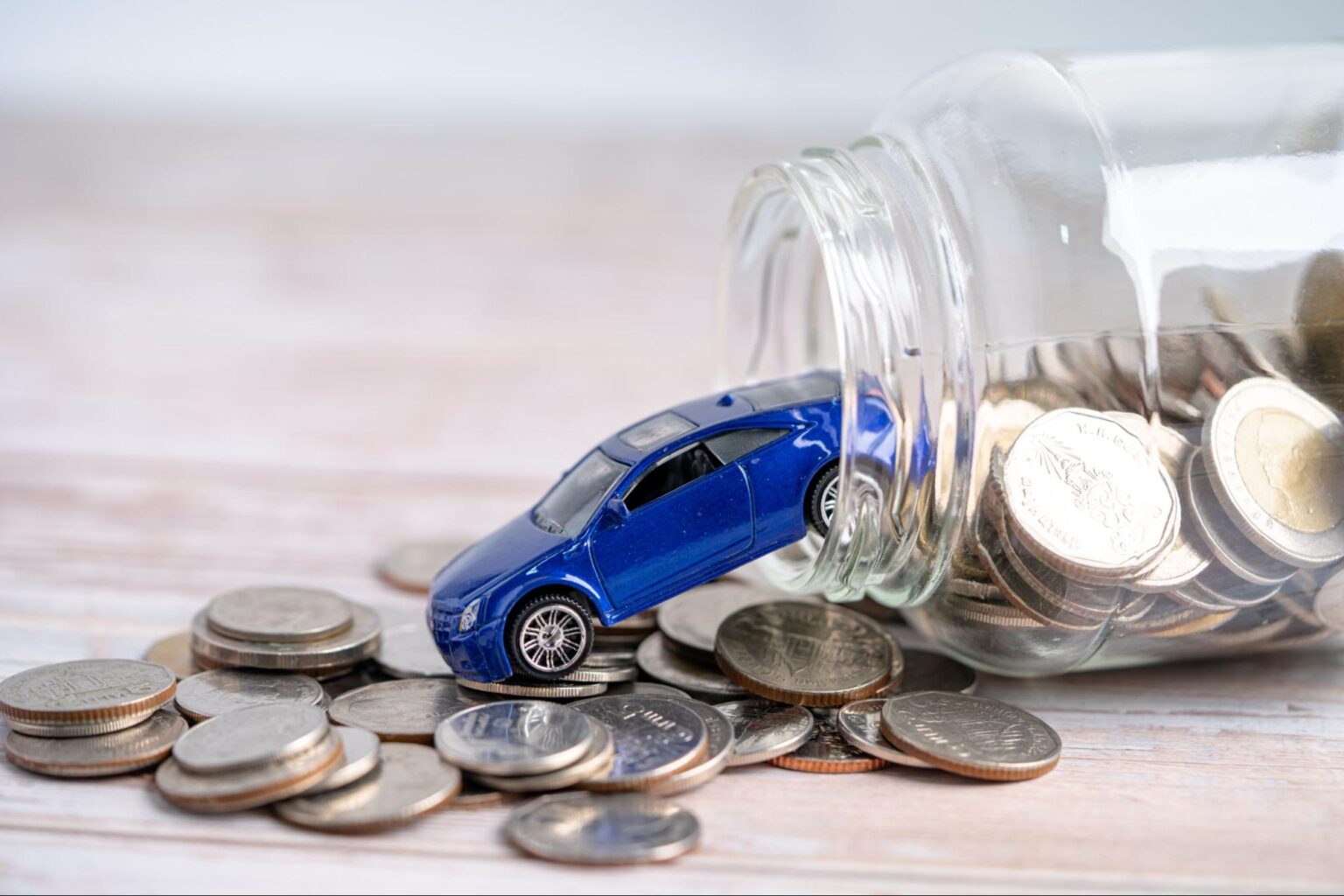 Blue toy car spilling coins from a savings jar for fun money saving.