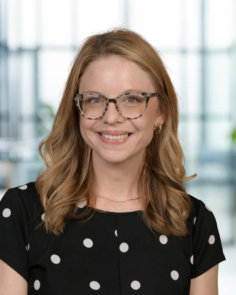 Smiling woman with glasses in a polka dot dress, showcasing a joyful expression.