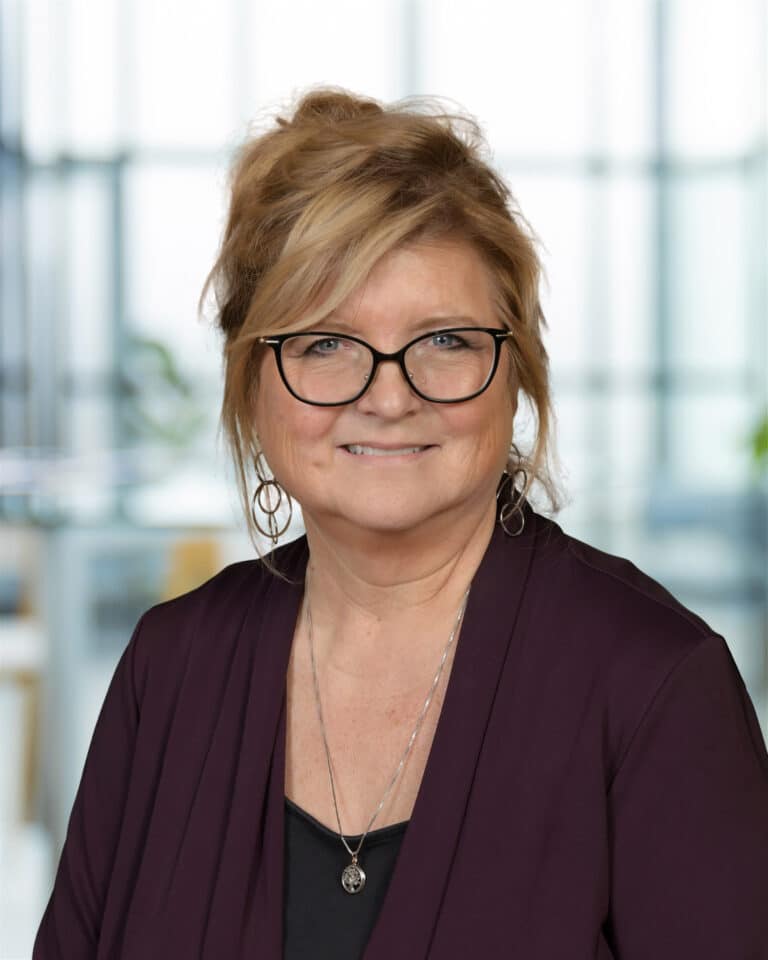 Professional woman smiling in a modern office environment with soft natural lighting.