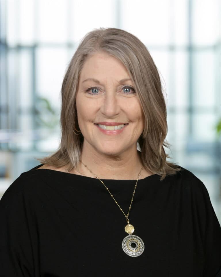 Smiling woman in a black top with stylish jewelry against a modern backdrop.