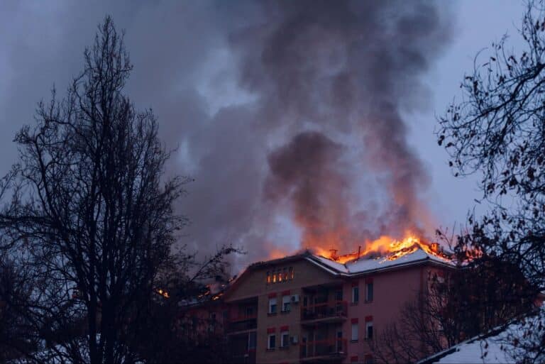 Flames engulf building at night, accompanied by thick smoke and glowing embers.