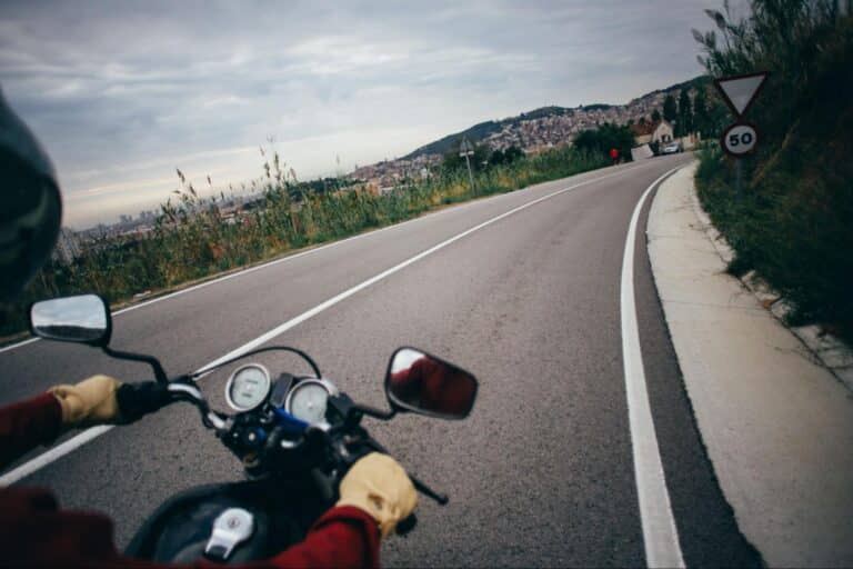 Motorcyclist navigating a scenic winding road through lush greenery and hills.