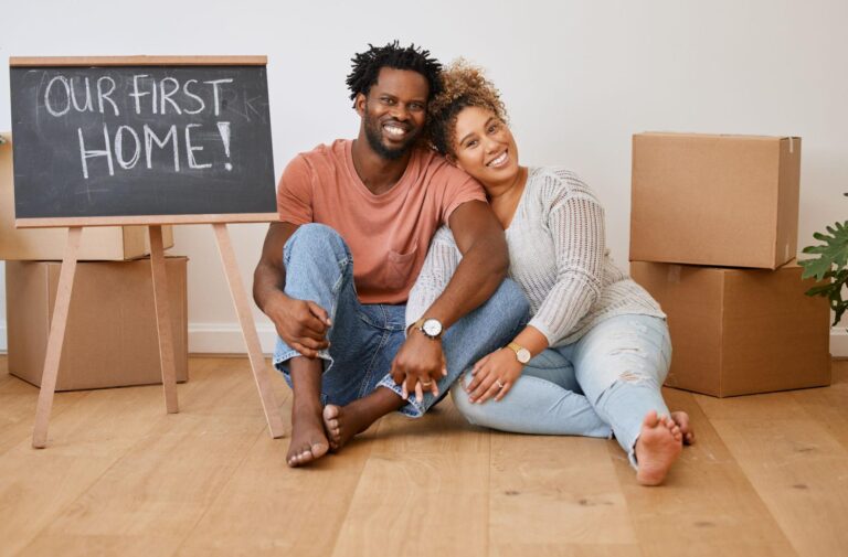 Happy couple celebrating their first home together with moving boxes and a chalkboard sign.