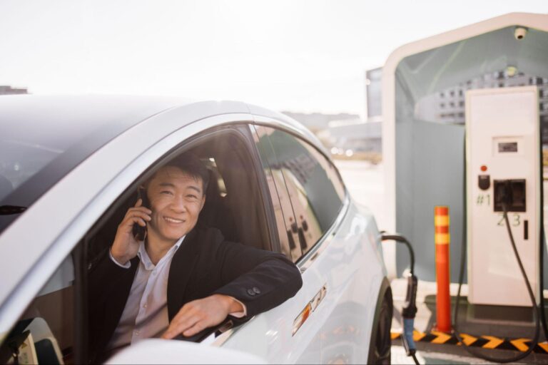 Man charging an electric vehicle while talking on the phone at a charging station.