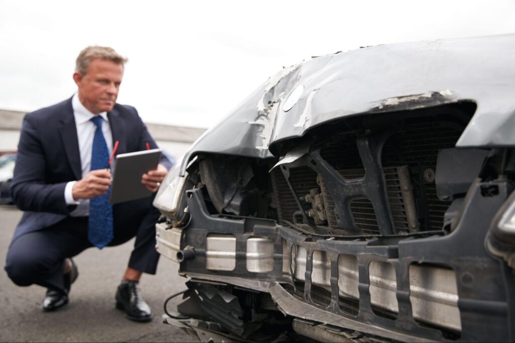 Business professional inspecting a damaged car for insurance assessment.