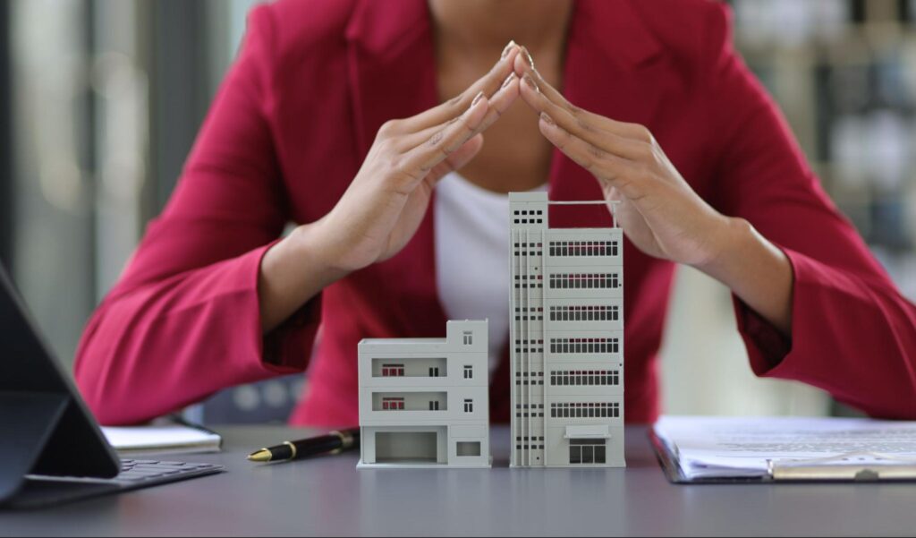 Businesswoman protecting model buildings with hands, symbolizing real estate investment and growth.