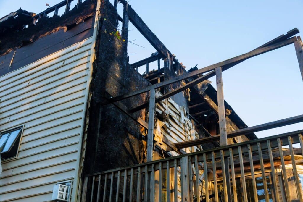 Severely burned house exterior with missing walls and structural damage from fire.