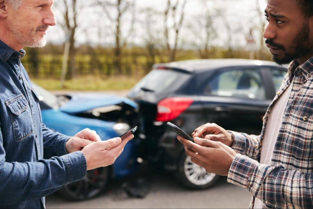 Two drivers exchanging information for insurance after a minor car accident on the road.
