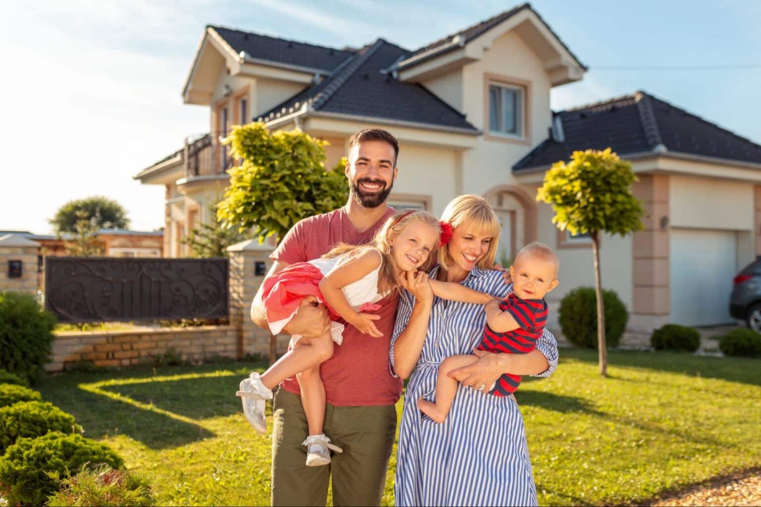 Happy family posing outside their beautiful home in the sunshine.