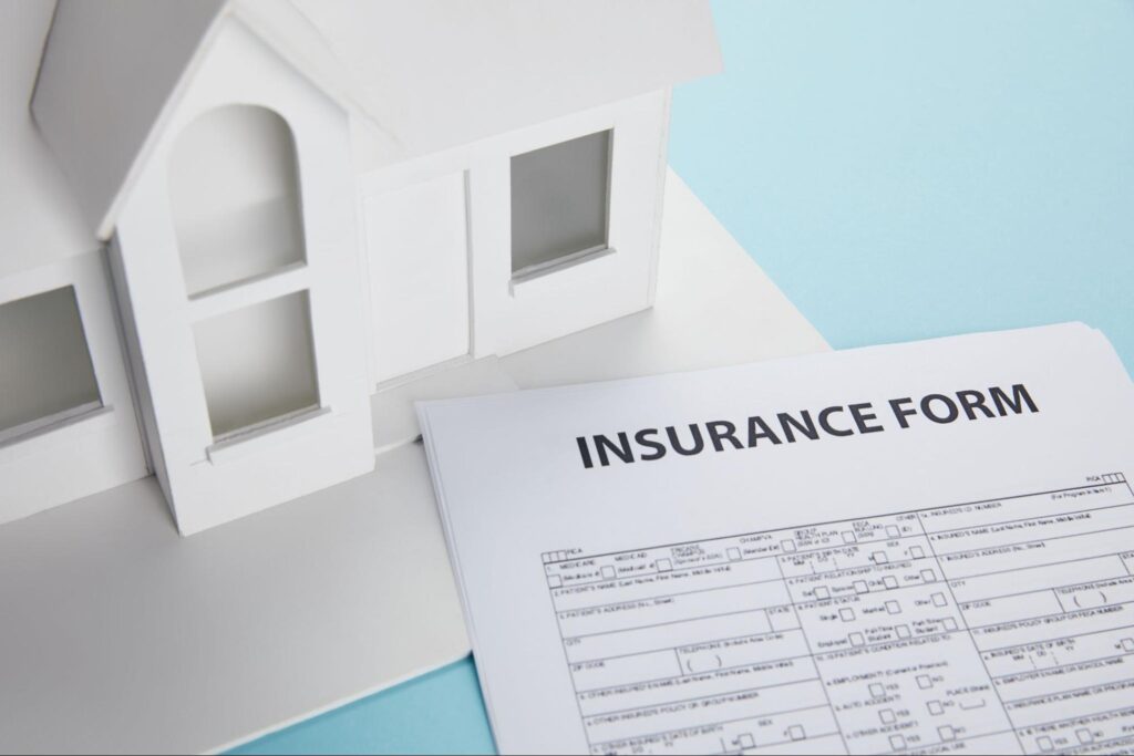Insurance form next to a model house on a blue background.