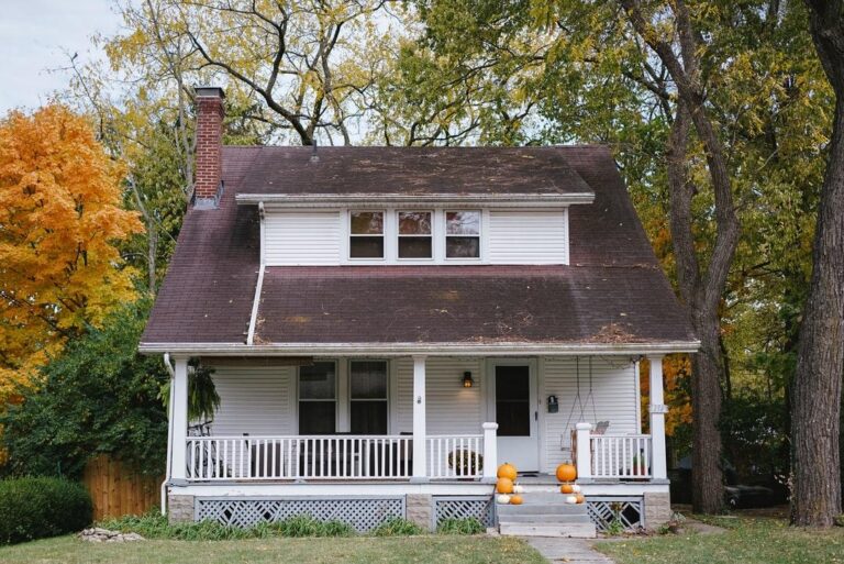 Charming white house with autumn foliage and pumpkins on the porch.