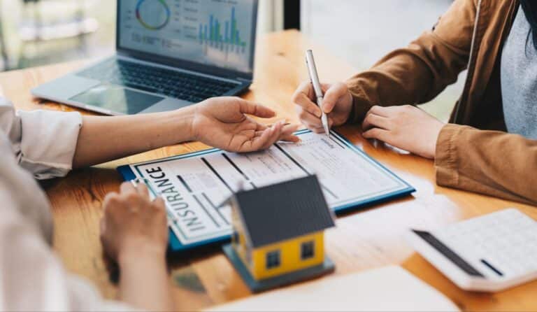 Homeowners signing insurance documents at a stylish desk with a miniature house model.