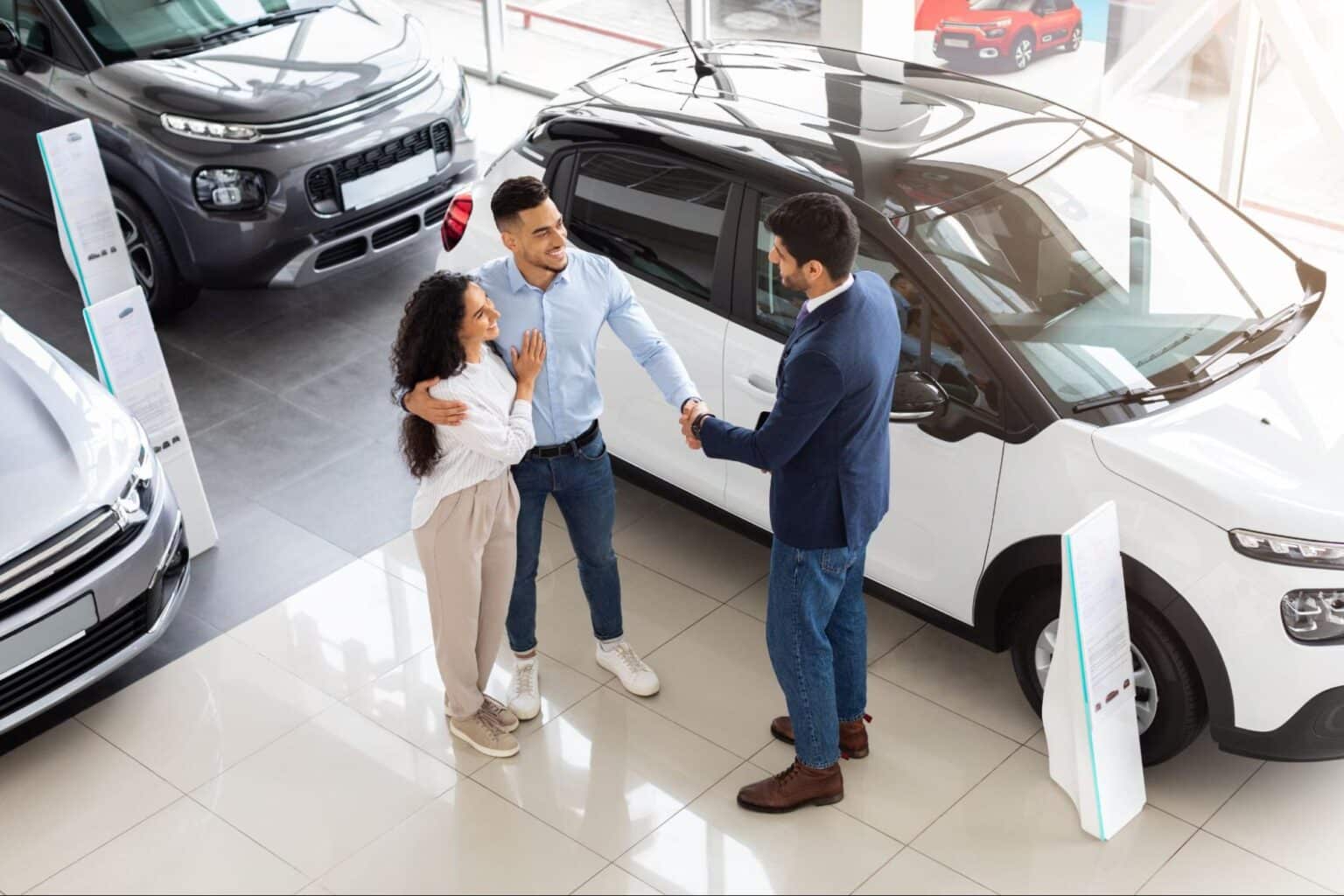 Couple excitedly completing their car purchase with a dealership representative.