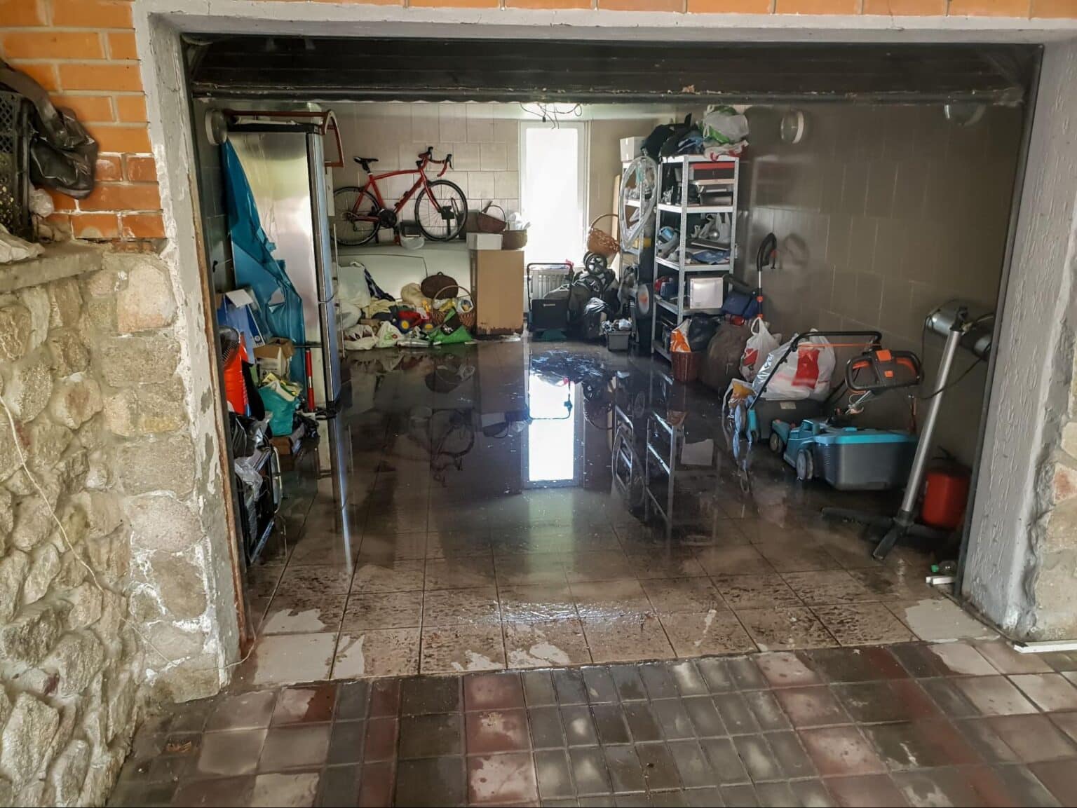 Flooded garage cleanup after rain, showing water and scattered belongings.