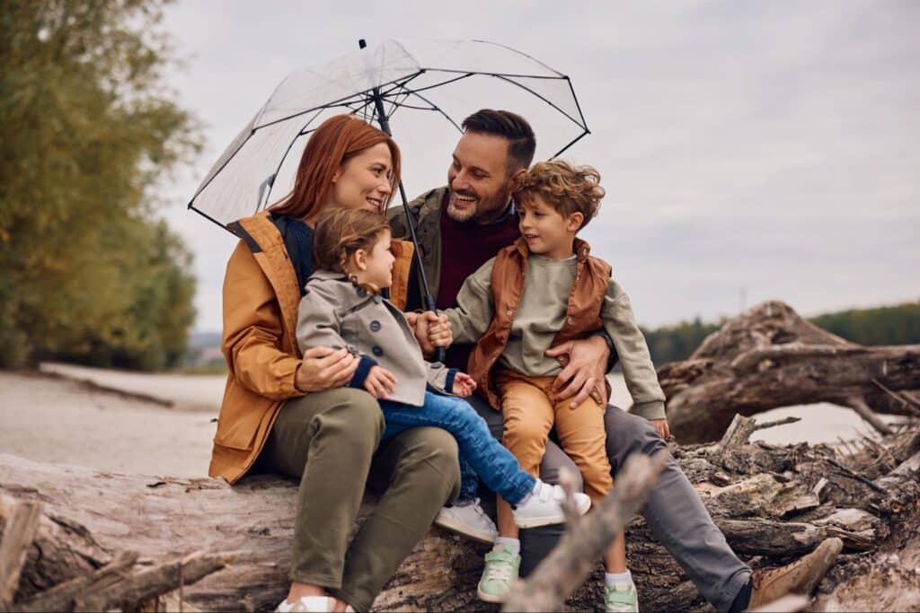 Family enjoying laughter under an umbrella by the water during a cozy outdoor moment.