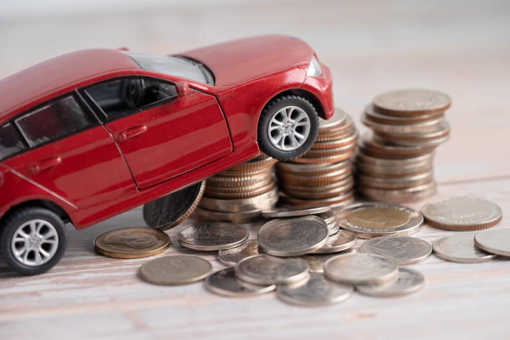 Red car atop coins, symbolizing car loans, financing, and saving money in insurance.