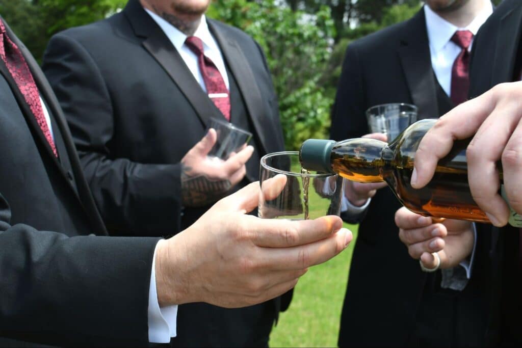 Groomsmen toasting with whiskey outdoors at a joyful wedding celebration.
