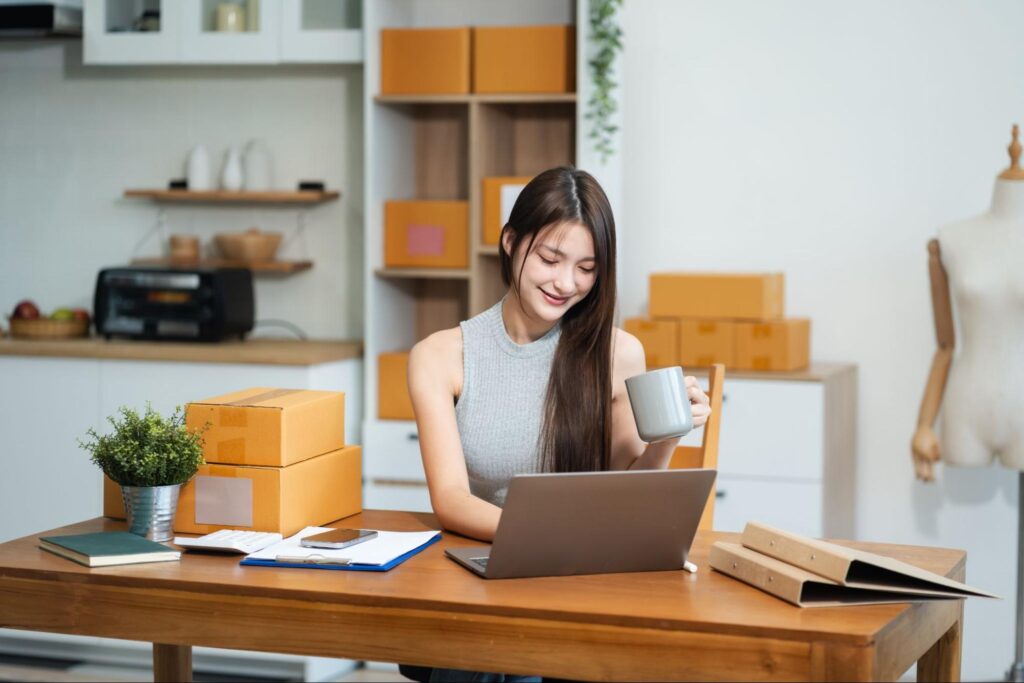 A woman sipping coffee while working on a laptop in a modern home office.